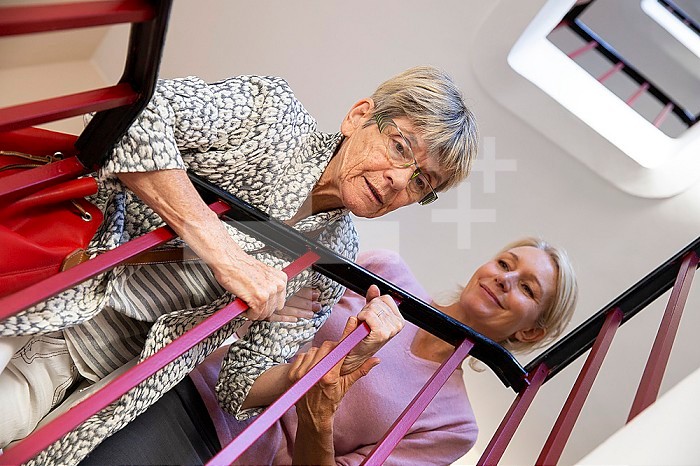 Elderly woman being helped by another woman to climb the stairs.