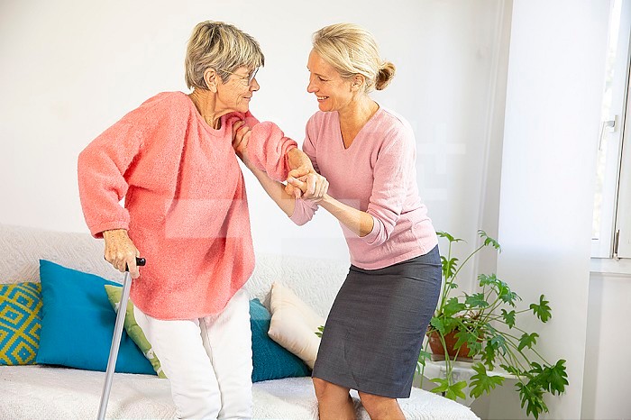 A woman in her fifties helping an elderly woman to stand up.