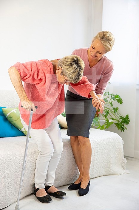 A woman in her fifties helping an elderly woman to stand up.