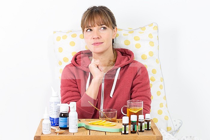 Young woman in bed hesitating between industrial medecine and natural remedies.