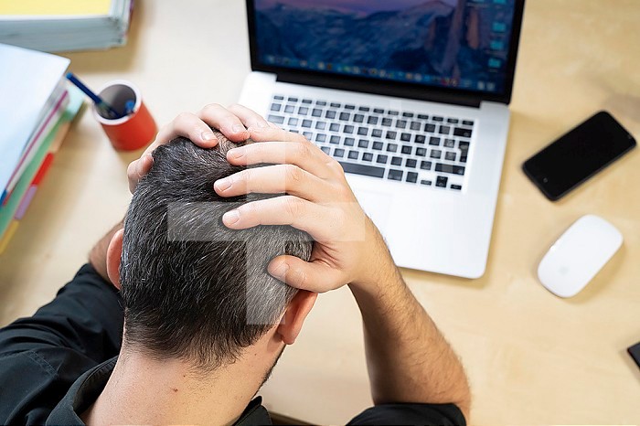 Man holding his head in his hands in front of his computer.