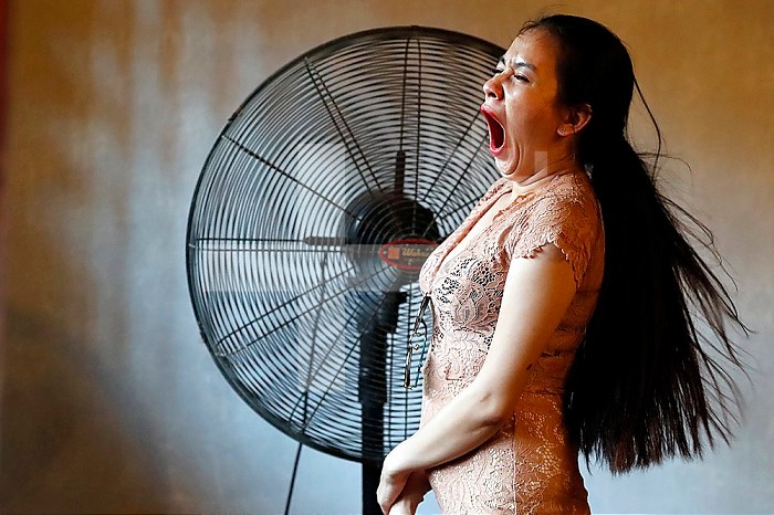 Tired and bored woman yawing in front of giant fan. Hanoi. Vietnam.