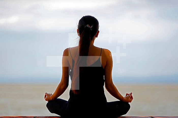 Silhouette of woman meditating in a lotus yoga position in front of the sea. Kep. Cambodia.