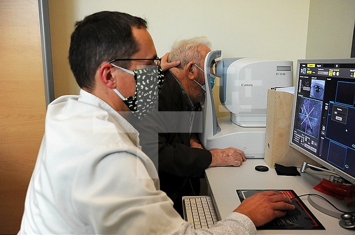 Ophthalmology office. Masked patient and doctor - Covid 19. Scan of the retina, an examination that allows you to precisely visualize the different parts of the eye. This imaging makes it possible to observe the retina in order to detect, for example, a retinal uplift with edema or a diabetic retinopathy. It is used to monitor wet AMD about every two months and complements the fundus to see if an injection of treatment is needed. OCT is also used to examine the optic nerve, and therefore screen for or monitor glaucoma.
