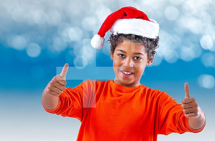 Teen boy in a Santa Claus hat shows two thumbs on a blue bokeh background
