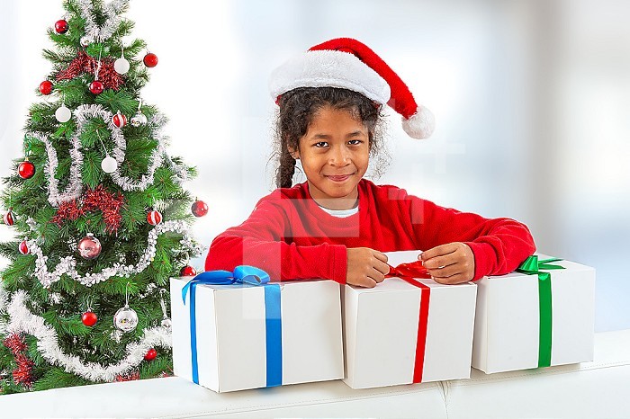 Merry Christmas and happy holidays. New Year 2020. Portrait of smiling cute little girl red T-shirt pajamas and Santa Claus hat holding gift box.