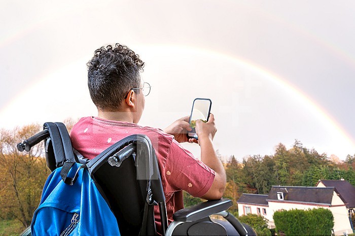 Teenager in a wheelchair facing a rainbow