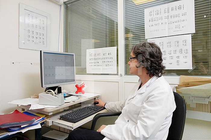 Cytogenetics laboratory, surrounded by karyotypes, a doctor analyzes the results of a sample in order to write a report.