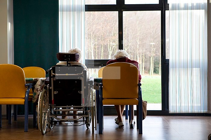 Two elderly people in a retirement home in front of a window.