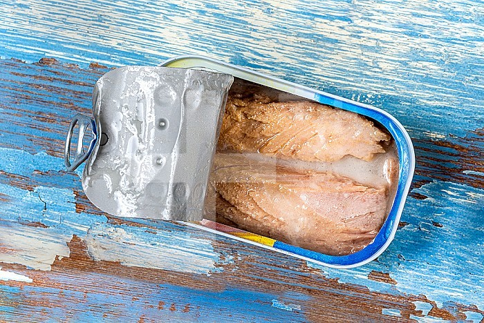 Open tuna can close up top view on blue stained background.
