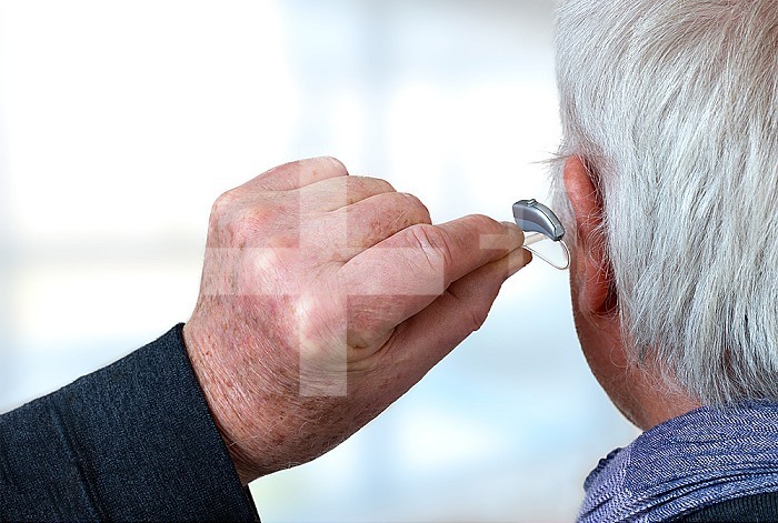 American shot of fitting a hearing aid to a white-haired senior citizen, rear view.