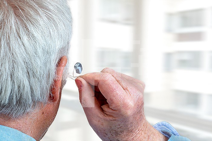 American shot of fitting a hearing aid to a white-haired senior citizen, rear view.