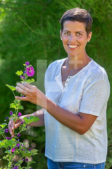 Young woman from the front holding a stem of hollyhocks.