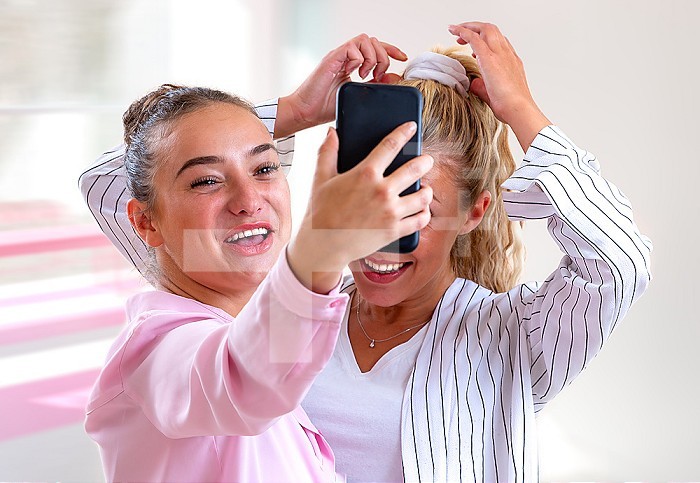 Two young women making a selfie laughing out loud - bright blurred background.