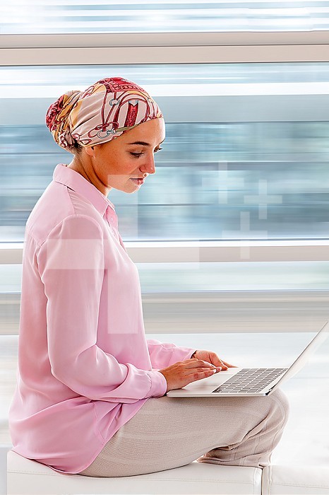 Young woman in profile wearing a headscarf, active, using a laptop computer