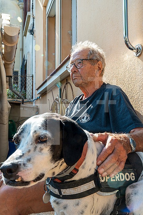 90 year old senior with his dog in the sun in front of his house.