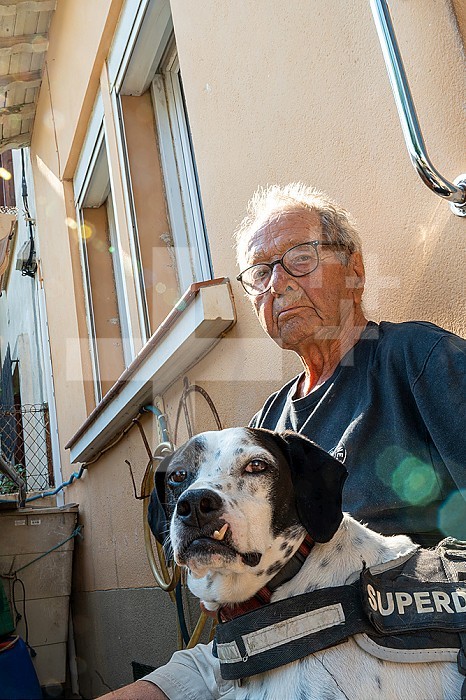 90 year old senior with his dog in the sun in front of his house.