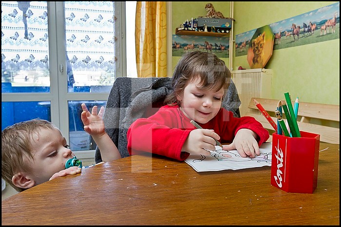 ASE - Childhood Social Assistance. Sarah, 3, draws at the table while Maxence tries to take the coloring book from her. EDITORIAL USES ONLY.