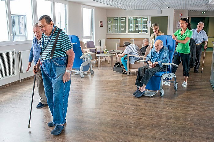 Deaf nurse pushing an elderly disabled resident in a wheelchair and accompanying deaf residents in the canteen.