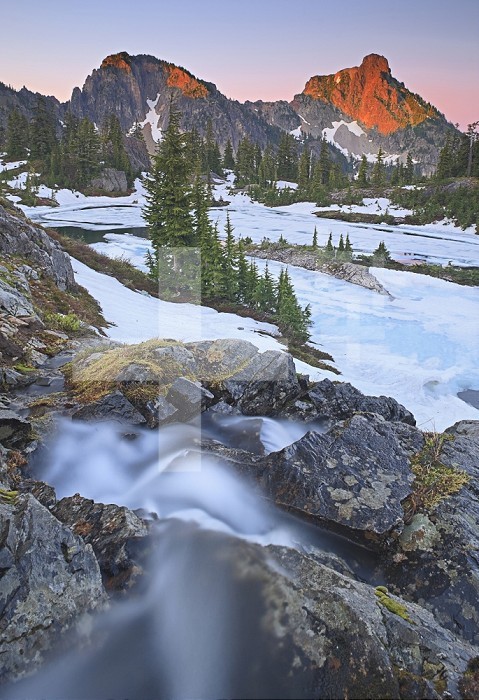 Alpenglow on Hibox Peak and Lila Lake with slowly melting snow in early July and a seasonal waterfall in the foreground, Alpine Lakes Wilderness, Cascade Range, Washington, USA.