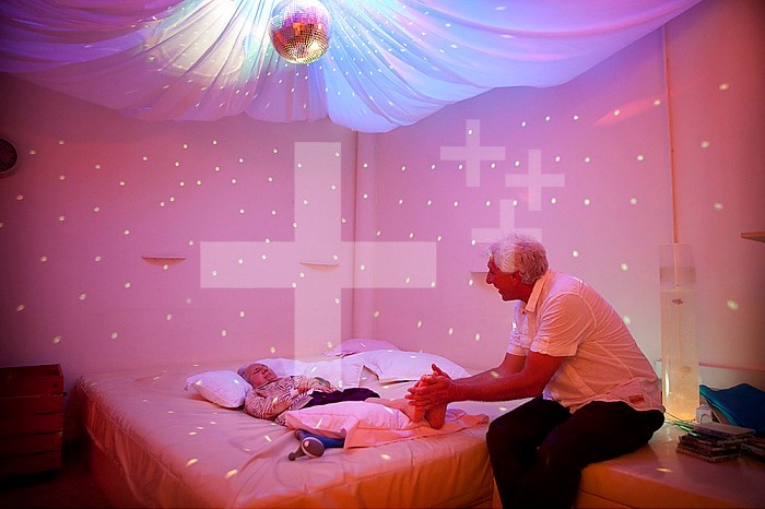 Reportage in a snoezelen room in Liege. Mony, 85, who has Alzheimer´s disease, moves around in this multi-sensory environment, which is both soothing and stimulating, with Marc Thiry, a physiotherapist specialising in psychomotor education. Professor Thiry has been following Mony since her disease was diagnosed 5 years ago. By stimulating the senses, these rooms allow people with Alzheimer´s, who, despite their disease, maintain a sensorial memory, to lower their anxiety levels. These rooms are as beneficial to the patients as to the medical staff, allowing a privileged relationship to be established between the two, and setting up means of communication other than speech. This room is equipped with a liquid oil disc lamp that has a relaxing, and even hypnotic effect, and a water bed heated to 37°c that plays music.