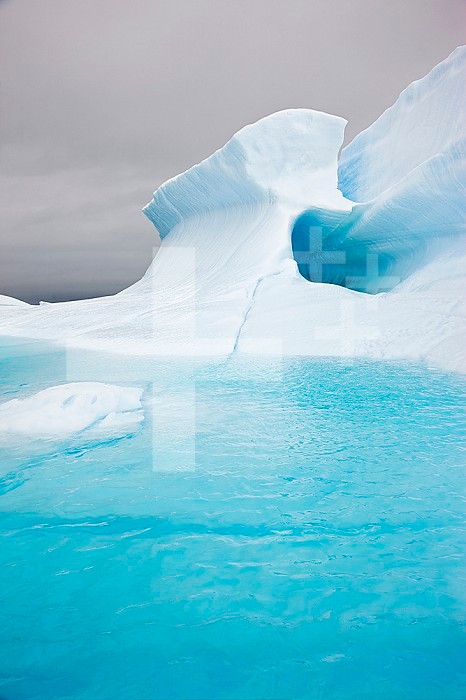 The blue ice of this iceberg is a result of the tremendous pressure imparted to the ice while it was still part of a massive glacier. Note the three states of water: liquid (ocean), solid (iceberg), and gas (cloud).