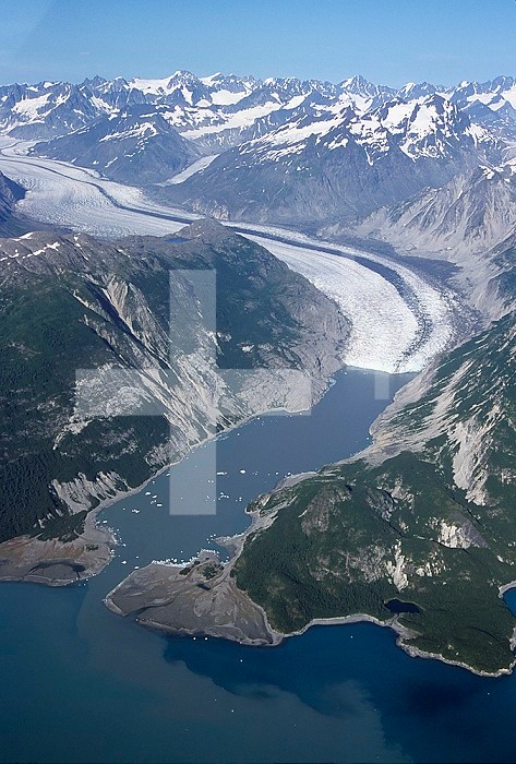 Glacier moving down a glacial valley into a fjord, Glacier Bay, Alaska, USA. Note the median and lateral moraines and some icebergs in the bay.
