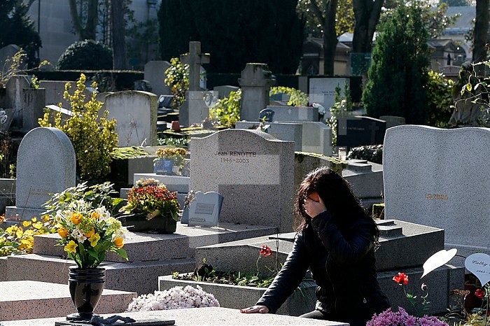 Woman praying at a grave in a cemetery.