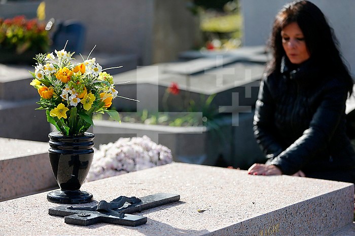 Woman praying at a grave in a cemetery.