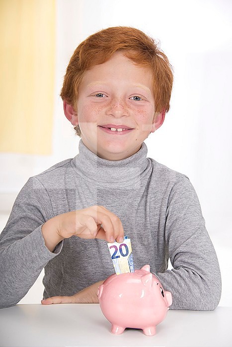 Boy putting banknote to piggybank.