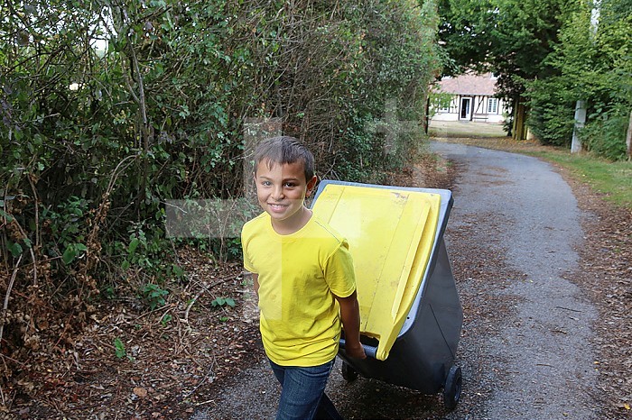 Boy pulling a recycling trash can.